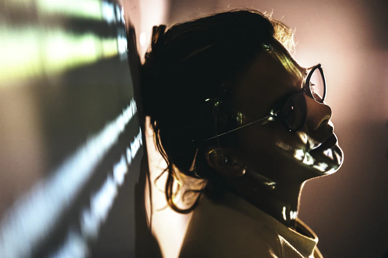 woman with glasses leaning head against wall