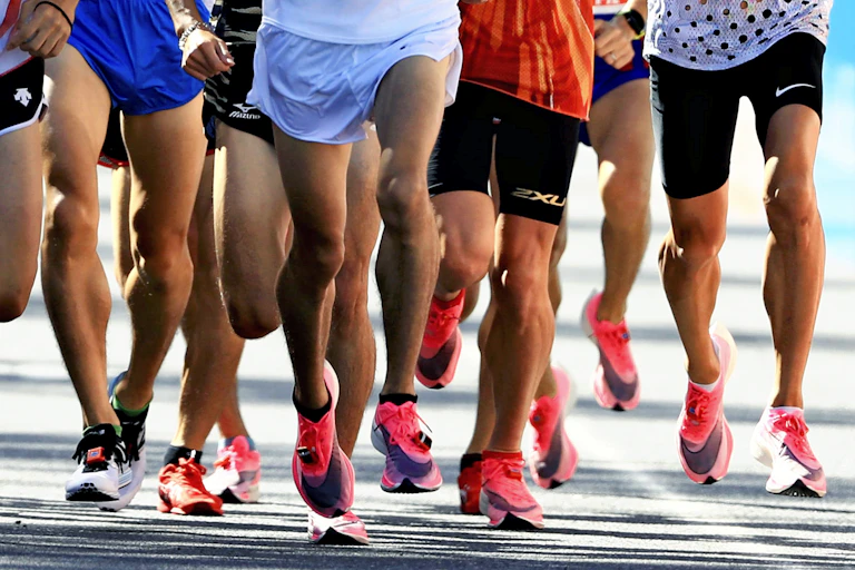 Action shot of a large group of people running, most wearing white and pink Nike shoes.