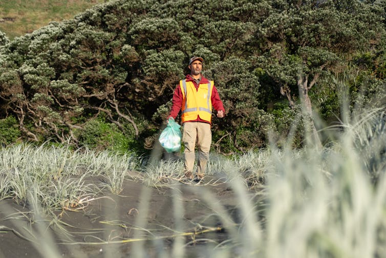 A man walking along a bech with a plastic bag full of rubbish