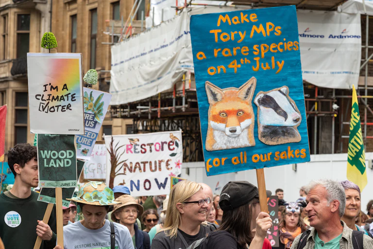 Placards in a march declare 'I'm a climate voter' and 'restore nature now'.