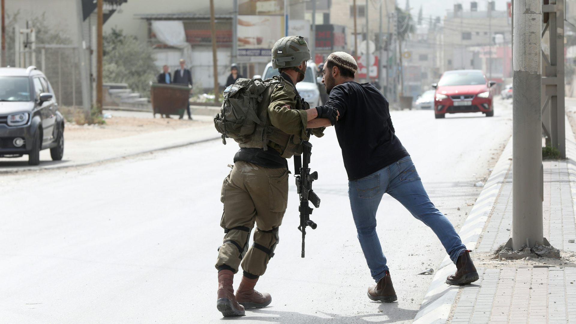 An Israeli soldier holds back a settler during a confrontation on the street.