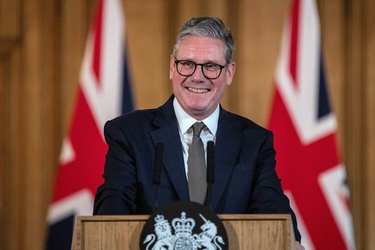 Keir Starmer standing at a podium in front of UK flags.