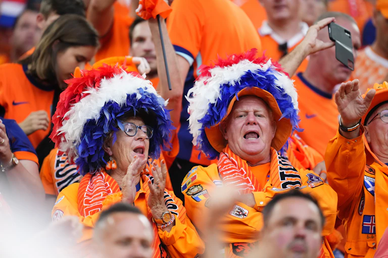 Soccer fans dressed in orange wear large feather hats.