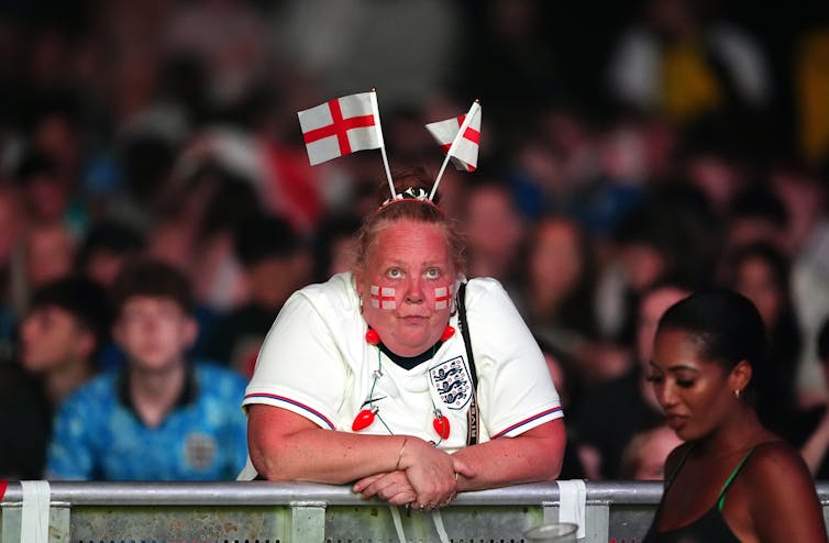 A woman with her face painted wears two English flags in her hair.