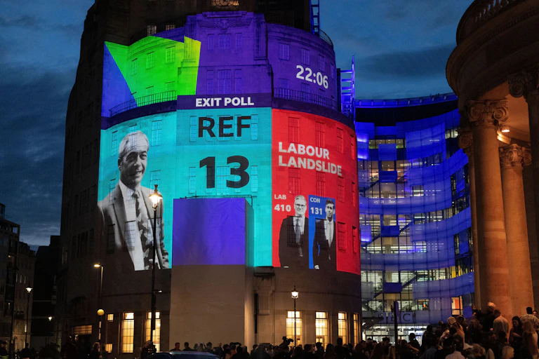 The 2024 exit poll projected onto the side of the BBC building in London while a crowd looks on.