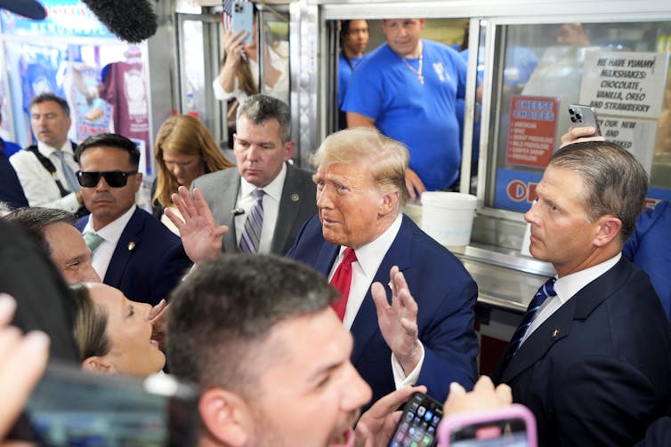 A man in a suit stands in a crowd, holding up his hands.