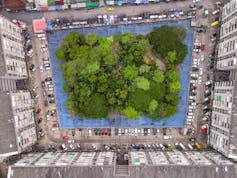 A huge apartment building, built in a square, with an urban forest in the middle