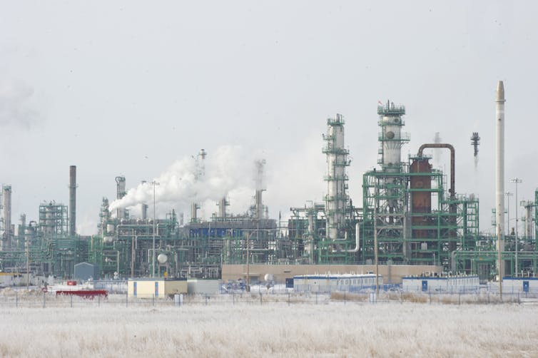 Smoke stacks billowing smoke seen next to prairie winter grass.
