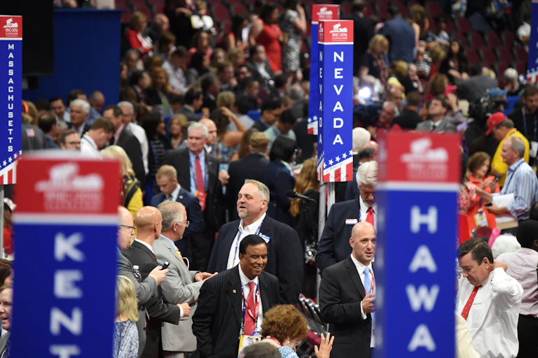 A crowd of people with tall pillars in red, white and blue with state names on them.
