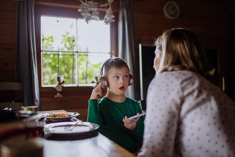 A boy wearing headphones interacting with his mother at home.