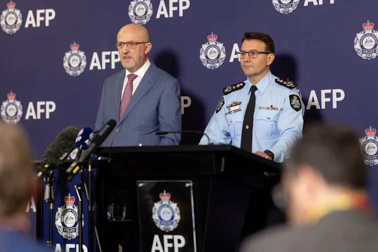Two men stand behind AFP branded lecterns and address the media