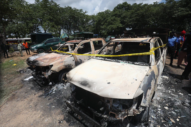 People in police uniform inspect burnt out vehicles.