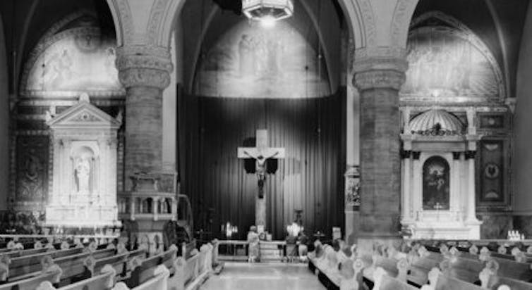 A black and white photograph of the inside of an ornate cathedral, with a crucifix in the middle.