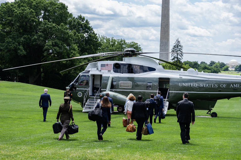 A group of people carry bags and walk toward an army green helicopter that says 'United States of America'