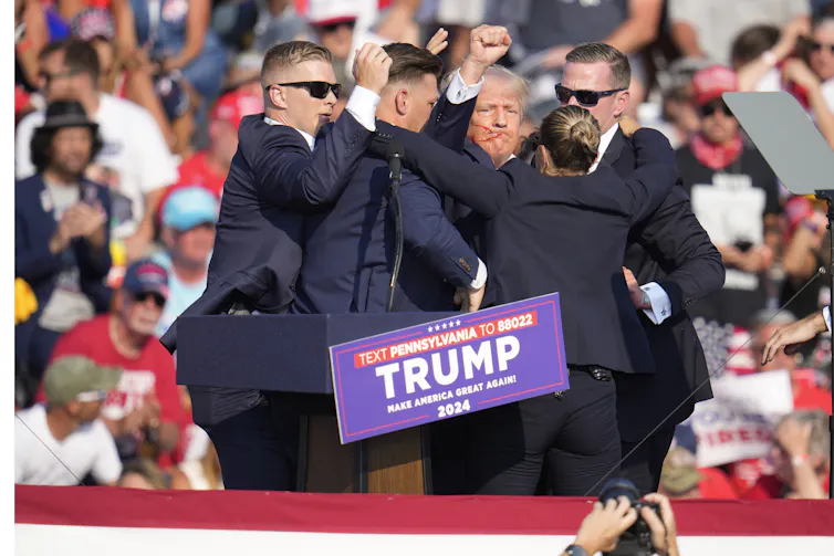 Trump, con la cara ensangrentada y el puño en alto, es conducido fuera del escenario
