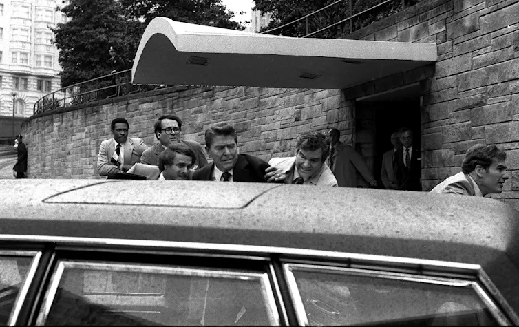 Foto en blanco y negro de Reagan siendo empujado a la limusina