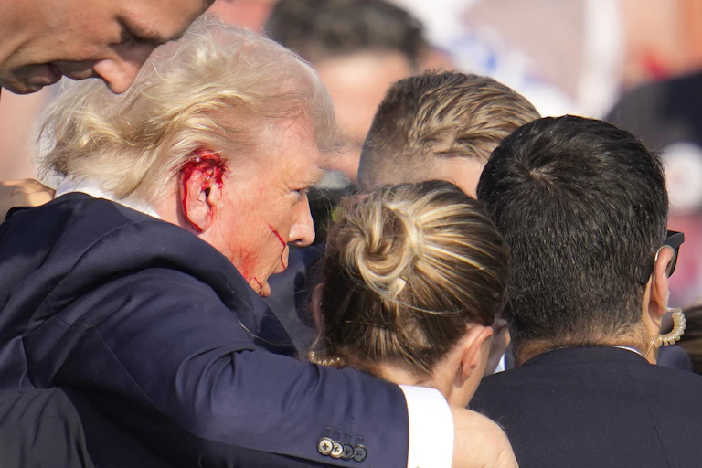 Trump has a bloody right ear as he is surrounded by Secret Service agents.