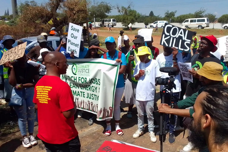 Protestors holding up placards saying 'coal kills', 'people-owned power', 'save our planet Earth' and 'march for jobs, clean energy, climate justice'