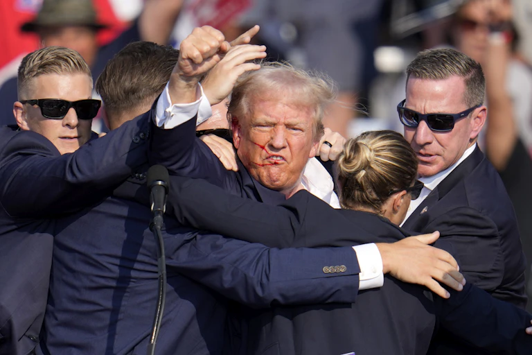 A man in a dark blue jacket, being pulled by several others, raises his fist.