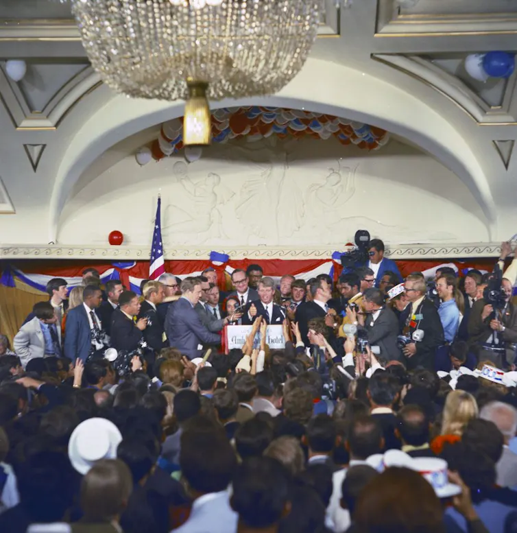 a man in a suit addresses a crowd in a ballroom