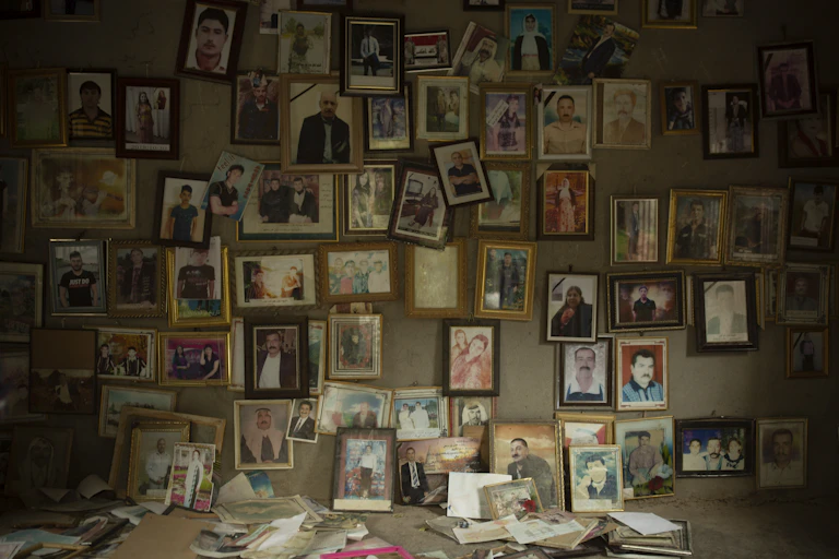 A wall of a darkened room, covered in small framed photographs.