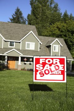 'Sold' sign on grass in front of a house