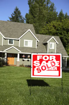 'Sold' sign on grass in front of a house