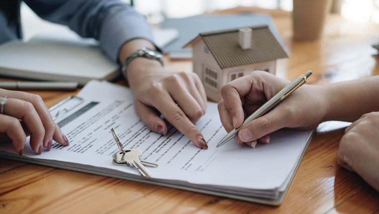 Closeup of hands signing contract, keys, model house.