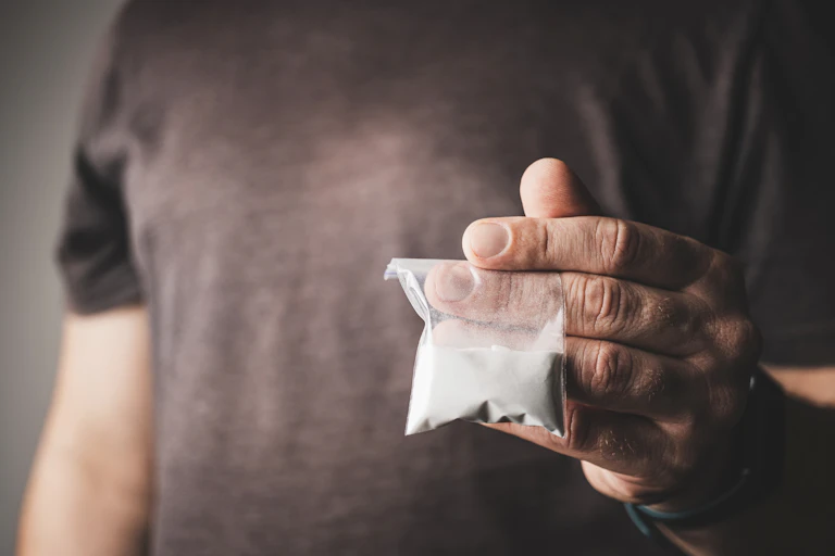 A person holds a small packet of white powder.