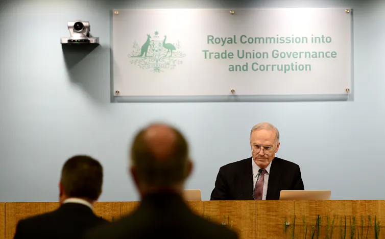 Man sitting behind raised desk speaking to people appearing before tribunal