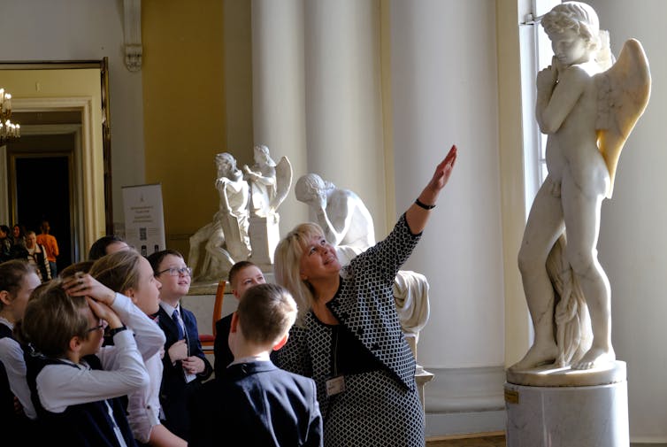 A class of children look at a naked statue.