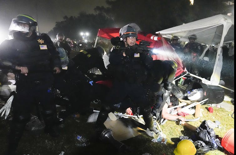 Nighttime shot of police in riot gear crowded around people lying on the ground