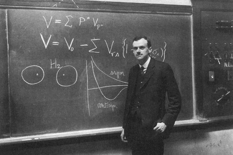 Portrait de Paul Dirac en noir et blanc, devant un tableau noir.