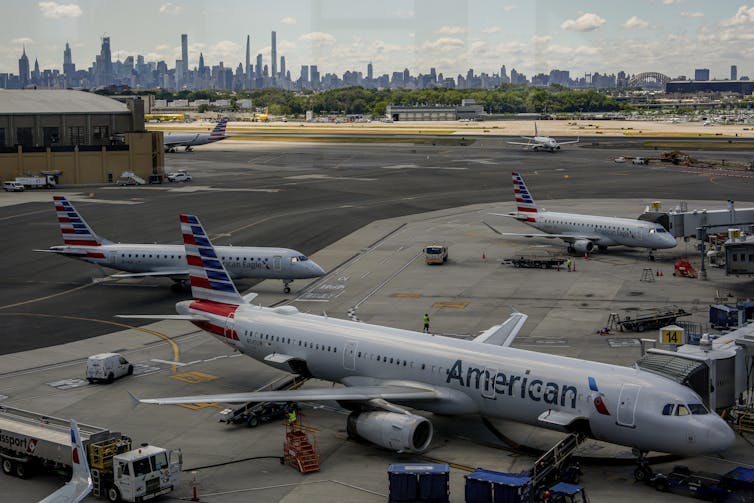 Airplanes parked on a tarmac with airport workers walking about.