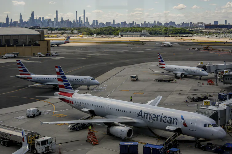 Airplanes parked on a tarmac with airport workers walking about.