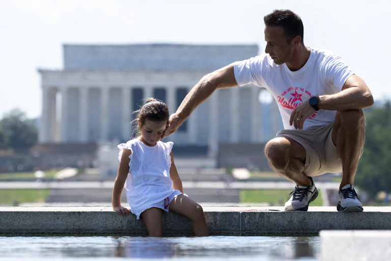 A man and a young girl are pictured in front of a monument.