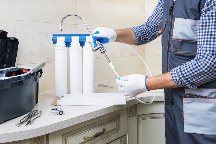 Man in work clothes installing a water filtration system in a kitchen