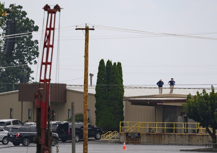 Two people are seen from a distance standing on top of a low lying, beige building.