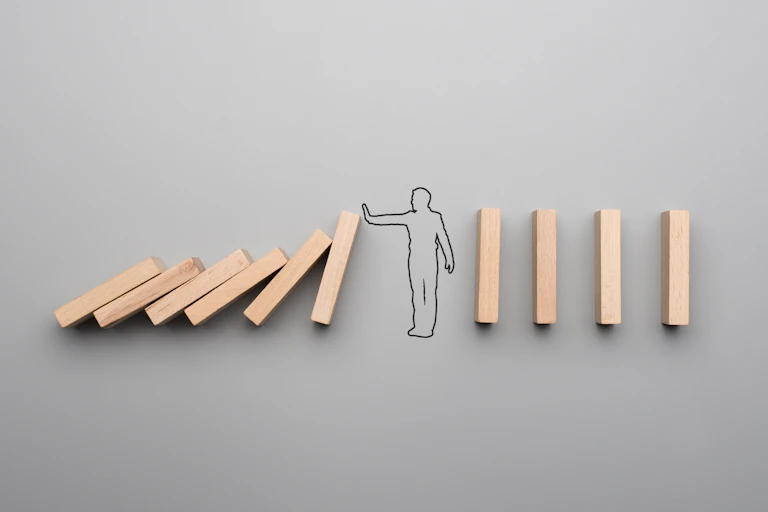 A row of dominoes collapses until it reachs a human figure holding up a hand to stop it.
