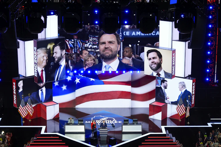 A giant video screen shows pictures of Vance