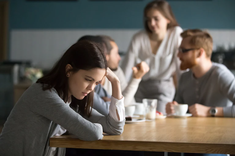 A group of young people sit round a table but one girl looks upset.