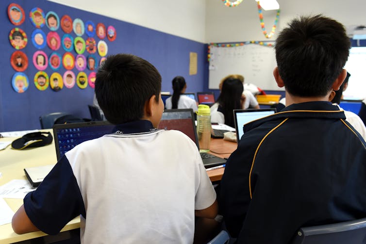 Two students sit at the back of a classroom, looking to the front.