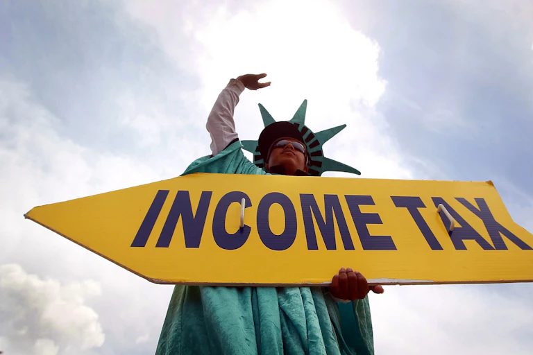 A man dressed as the Statue of Liberty holds a arrow sign reading "income tax"