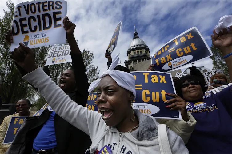 People outside the Illinois Capitol wave signs calling for a vote on the state's flat tax rate.