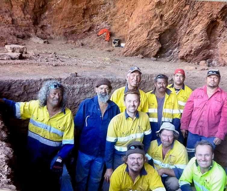 Photo of several men wearing high vis gear standing in front of a cliff.