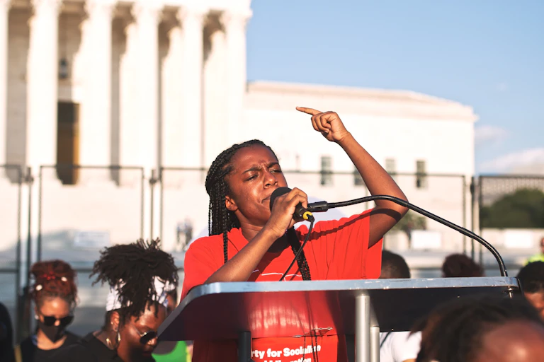 A Black woman speaks into a microphone in front of a crowd.
