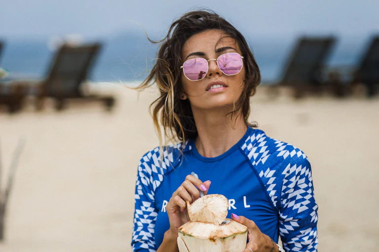 Une femme sur la plage se protège du soleil avec un vêtement conçu à cet effet et des lunettes de soleil.