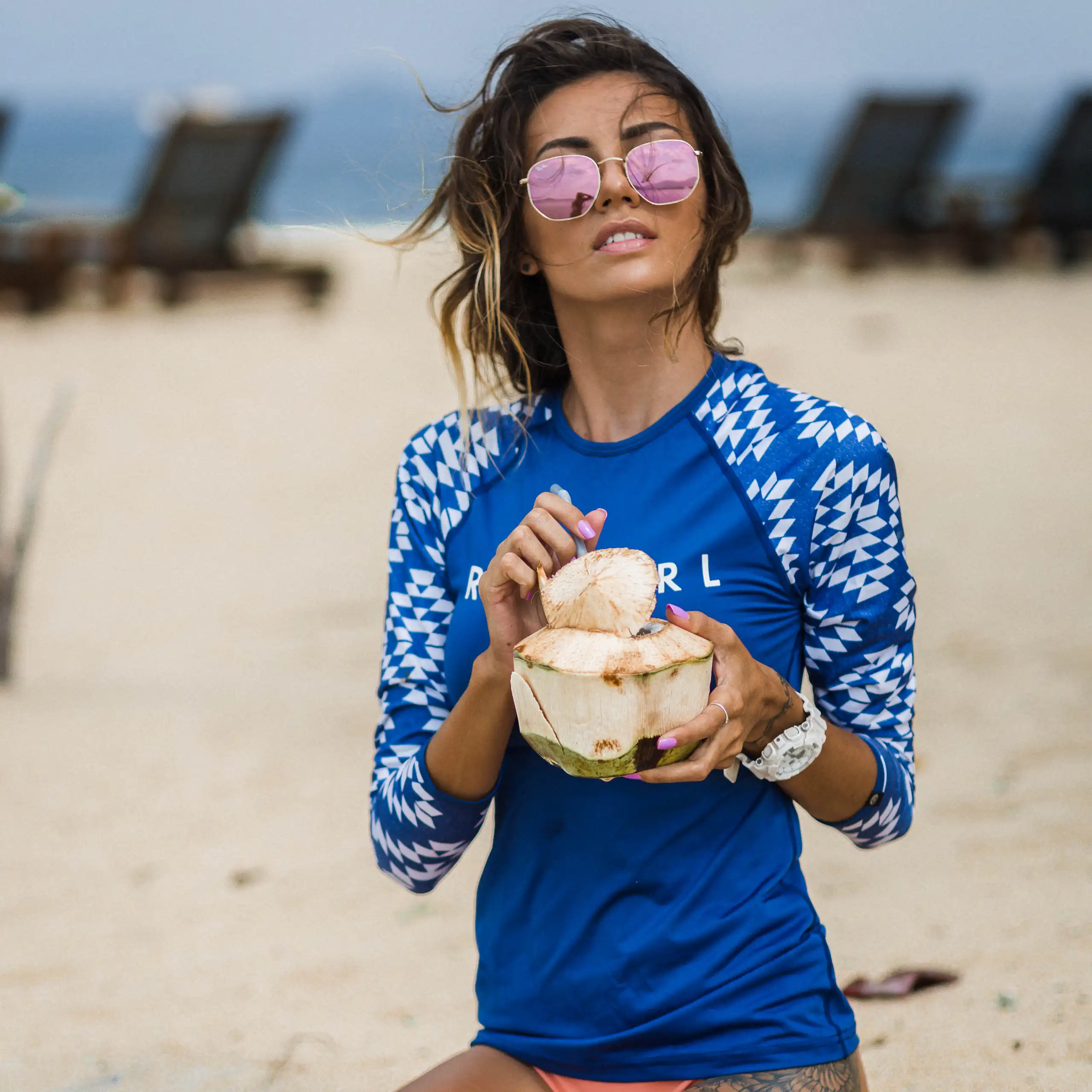 Une femme sur la plage se protège du soleil avec un vêtement conçu à cet effet et des lunettes de soleil.