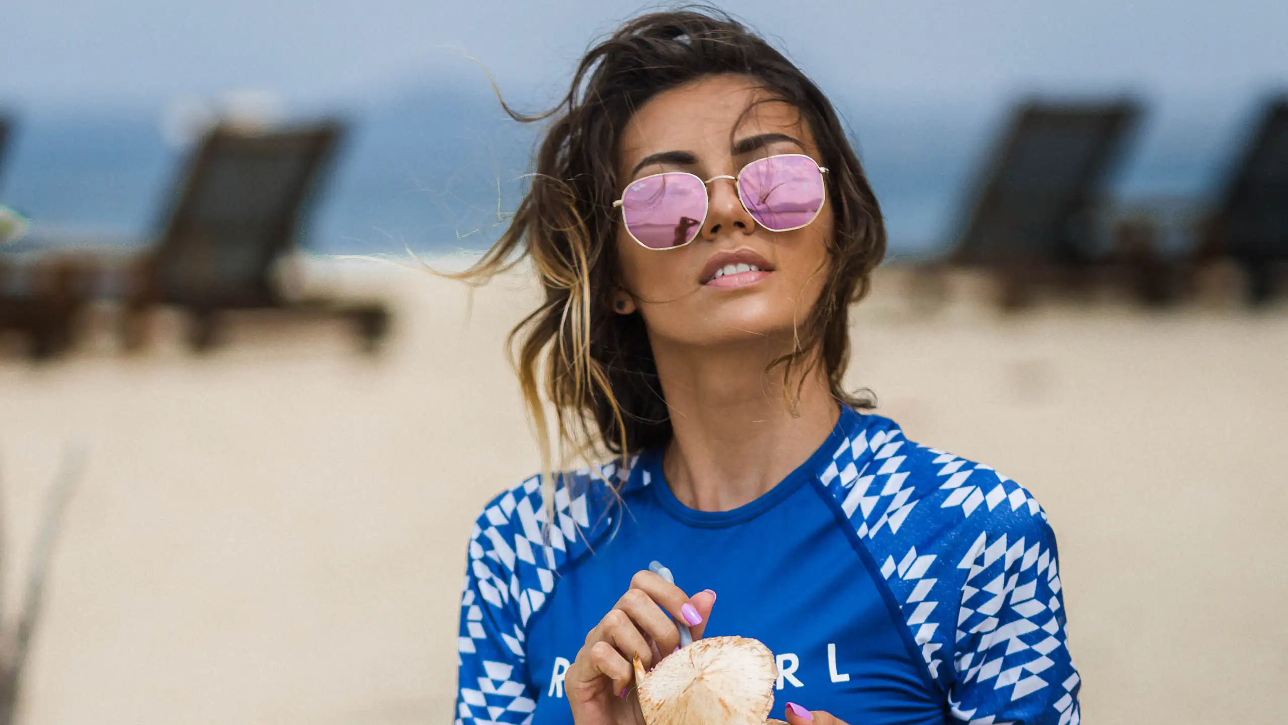 Une femme sur la plage se protège du soleil avec un vêtement conçu à cet effet et des lunettes de soleil.