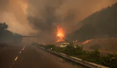 A fire blazes across a busy road in Cape Town with smog filling the air